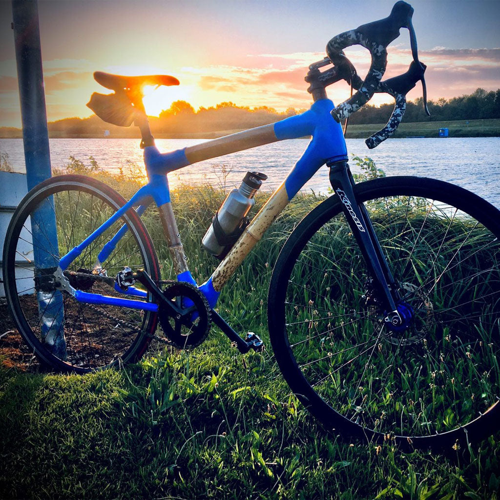 Andy's bamboo road bike with bright blue joints beside a lake, the low sun behind it
