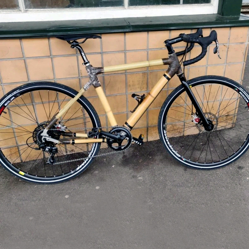 Frederik's bamboo road bike with dark wrapped joints and disc brakes, against a tiled wall