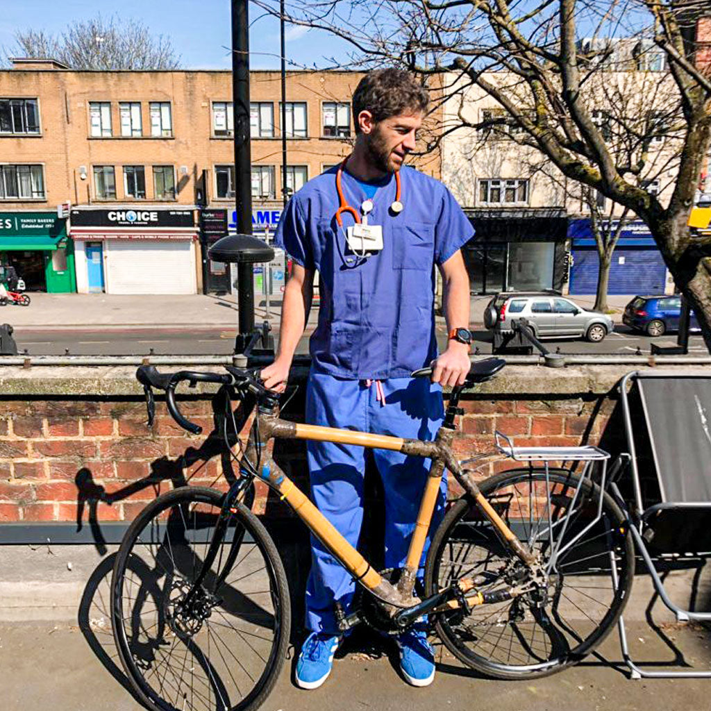 Rider behind Harry's bamboo road bike with black joints and a rear rack on a sunny city street