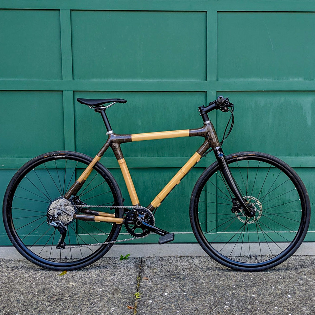 Rhys's bamboo city bike with dark joints and a flat handlebar, side view against a green garage door