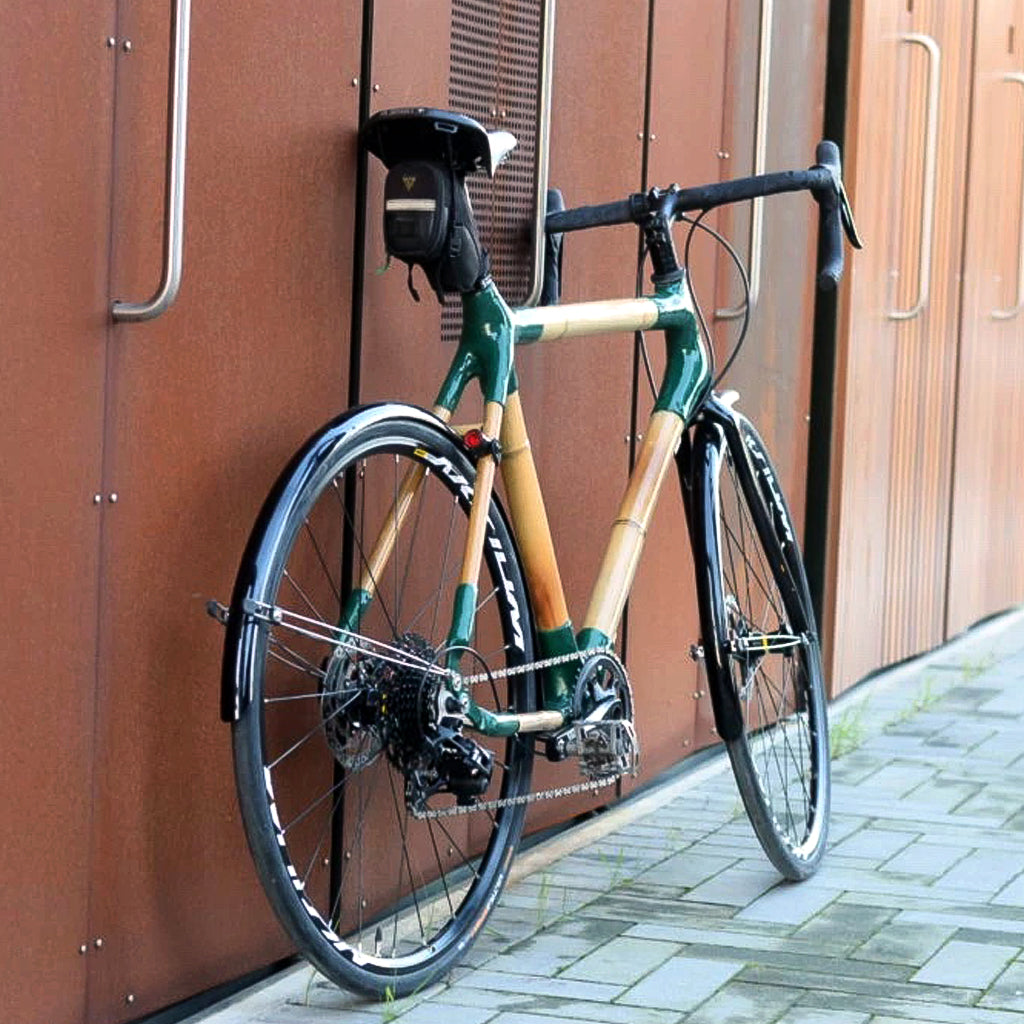 Doug's bamboo touring bike with dark green joints and full mudguards against a rust-coloured metal wall