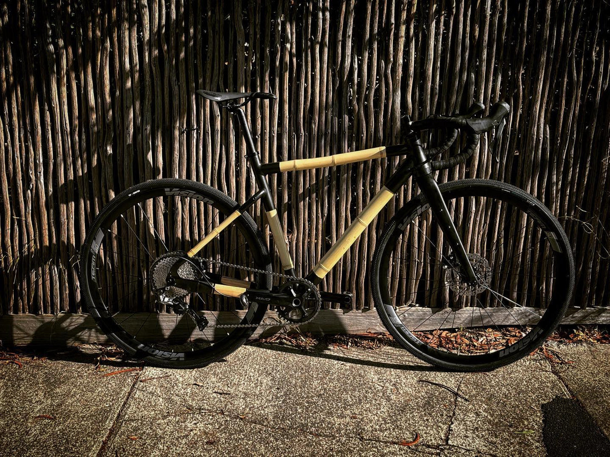 Jason's lugged bamboo gravel bike, built with the GRX finishing pack, against a reed fence in low sun