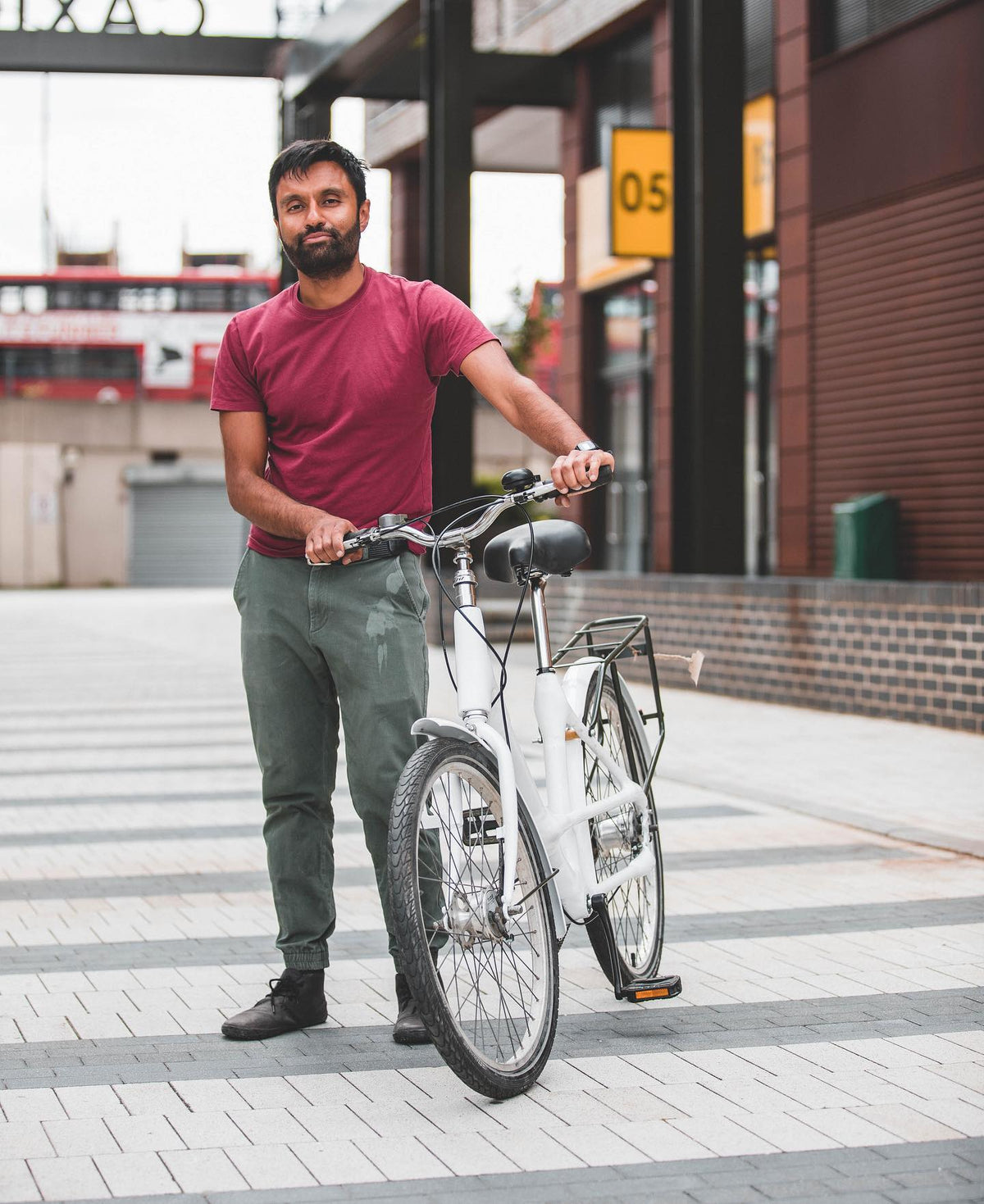 Rider holding a white step-through bike with a rear rack and mudguards on a paved street