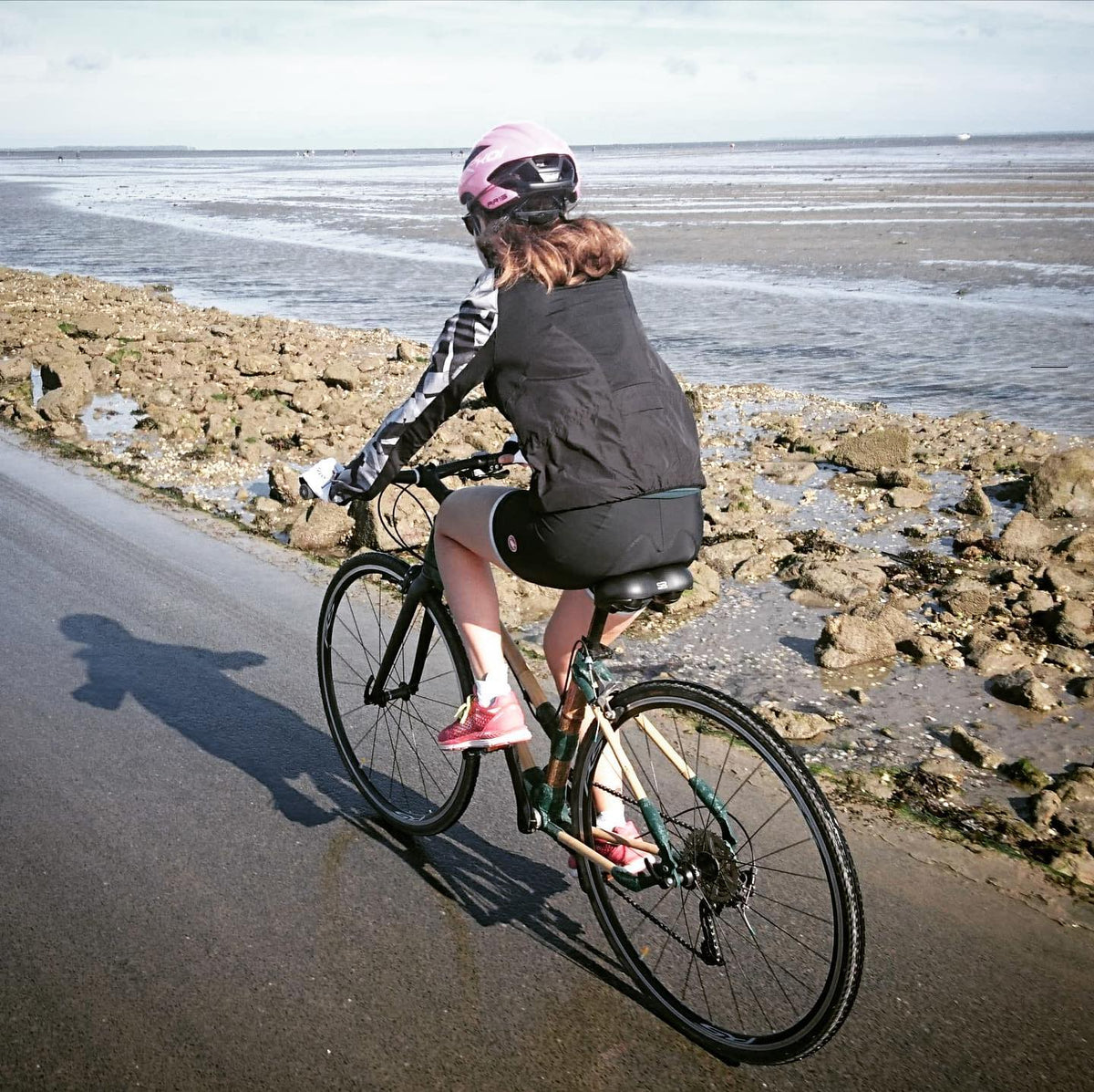Rider on a bamboo bike with green joints crossing the Passage du Gois causeway past tidal flats