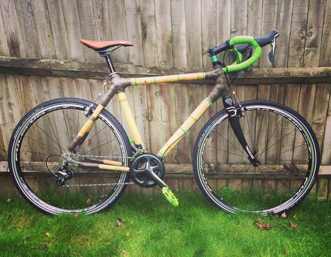 Austin's bamboo cyclocross bike with brown wrapped joints and green bar tape, against a wooden fence