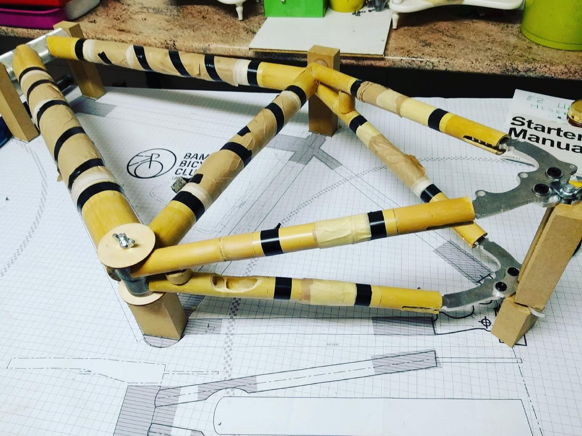 Bamboo gravel frame on jig blocks over the drawing, tubes banded with black tape, beside the starter manual