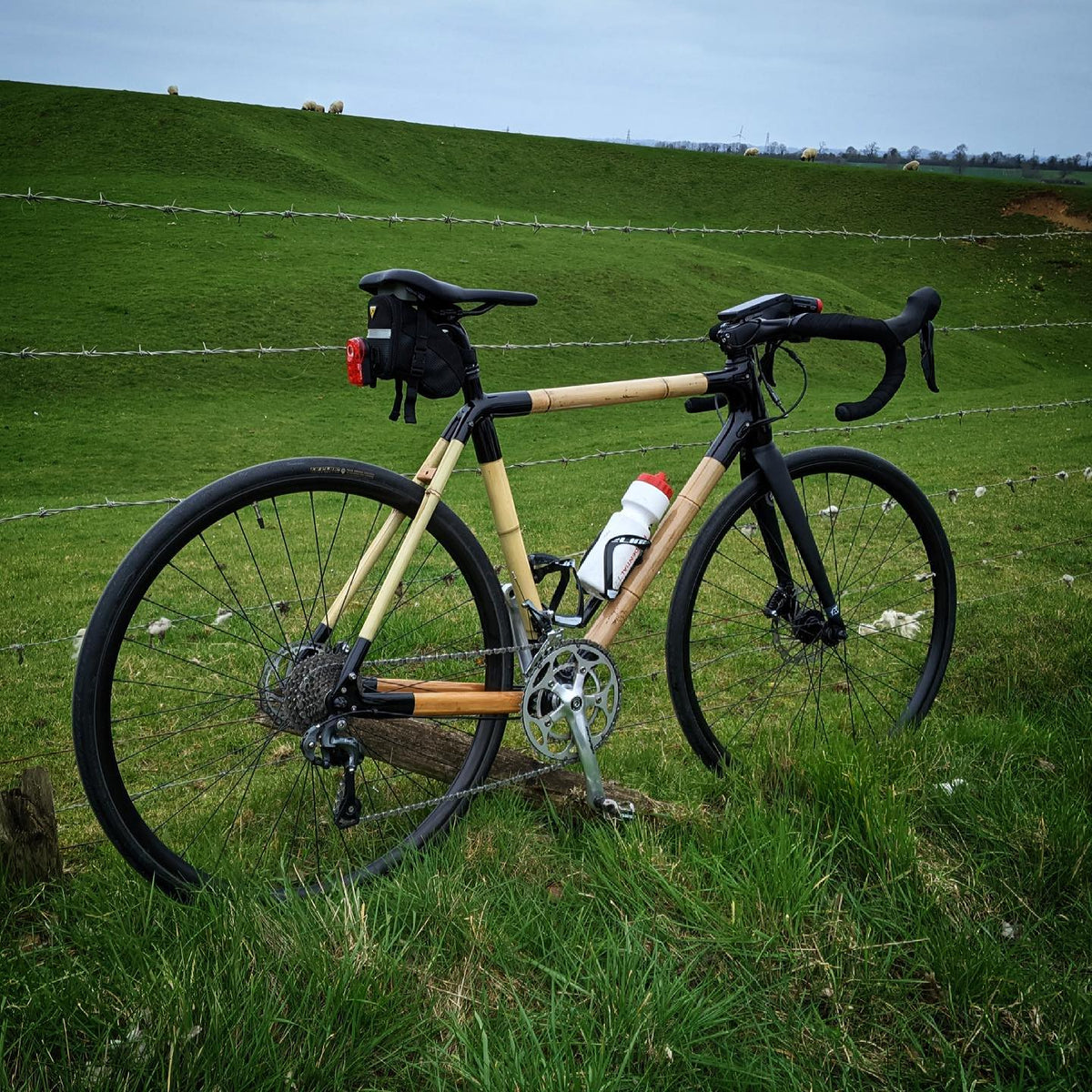 Robert's bamboo bike with a saddle bag and water bottle by a wire fence on a grassy hillside