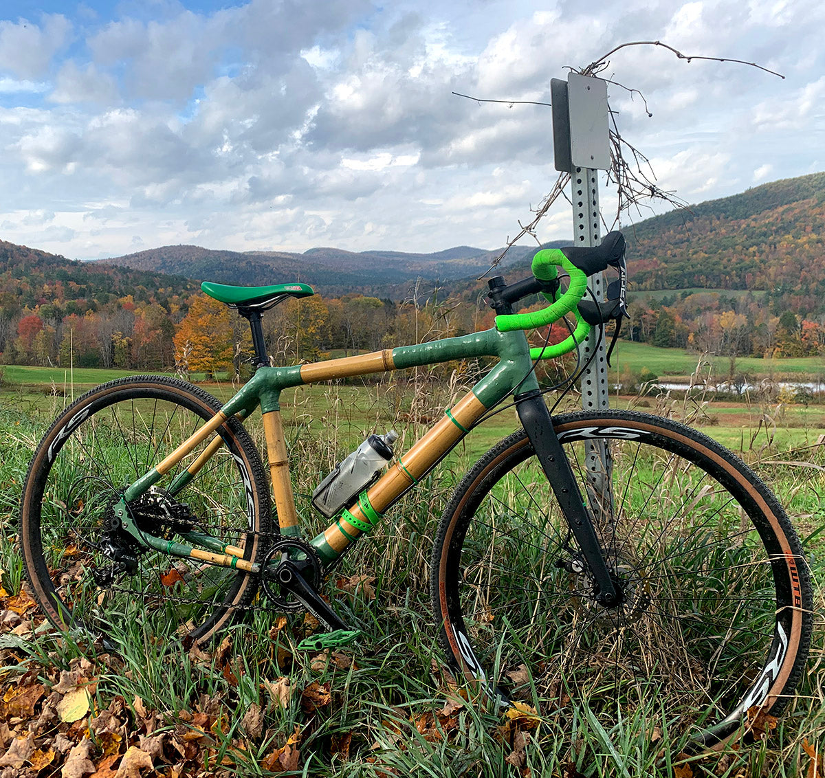 Will's bamboo gravel bike with green joints and bright green bar tape by a signpost below autumn hills