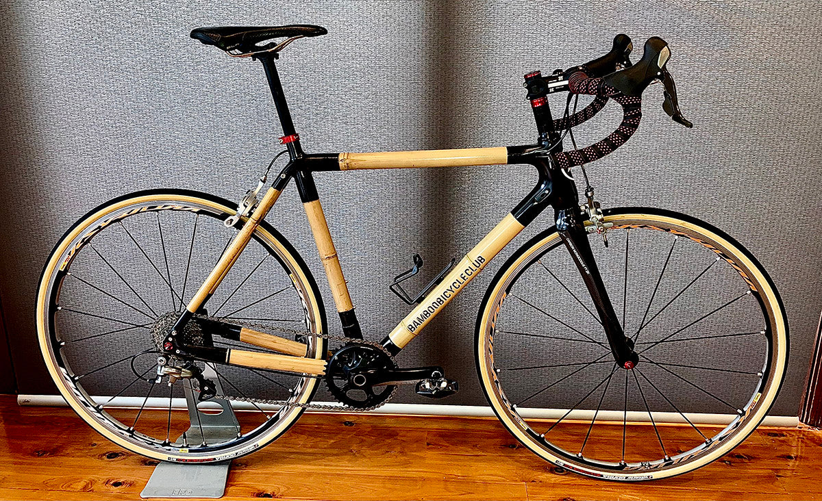 Mike's bamboo road bike with black joints and cream tyres on a stand against a grey wall