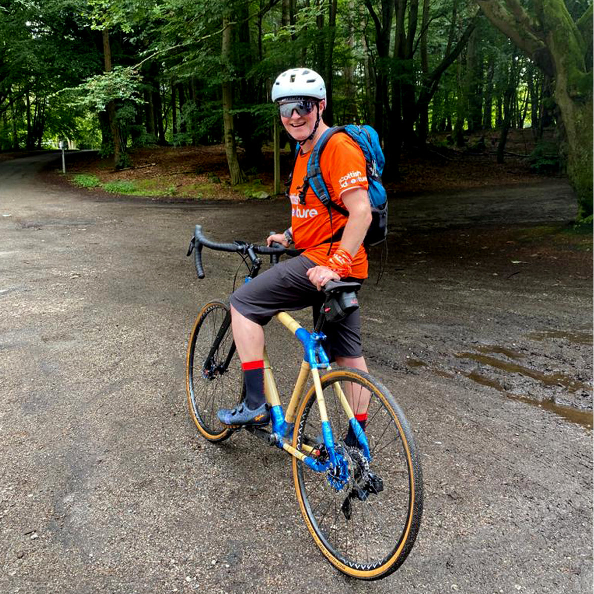 A rider sitting on Steve's bamboo gravel bike, with blue joints and tan-wall tyres, on a woodland track