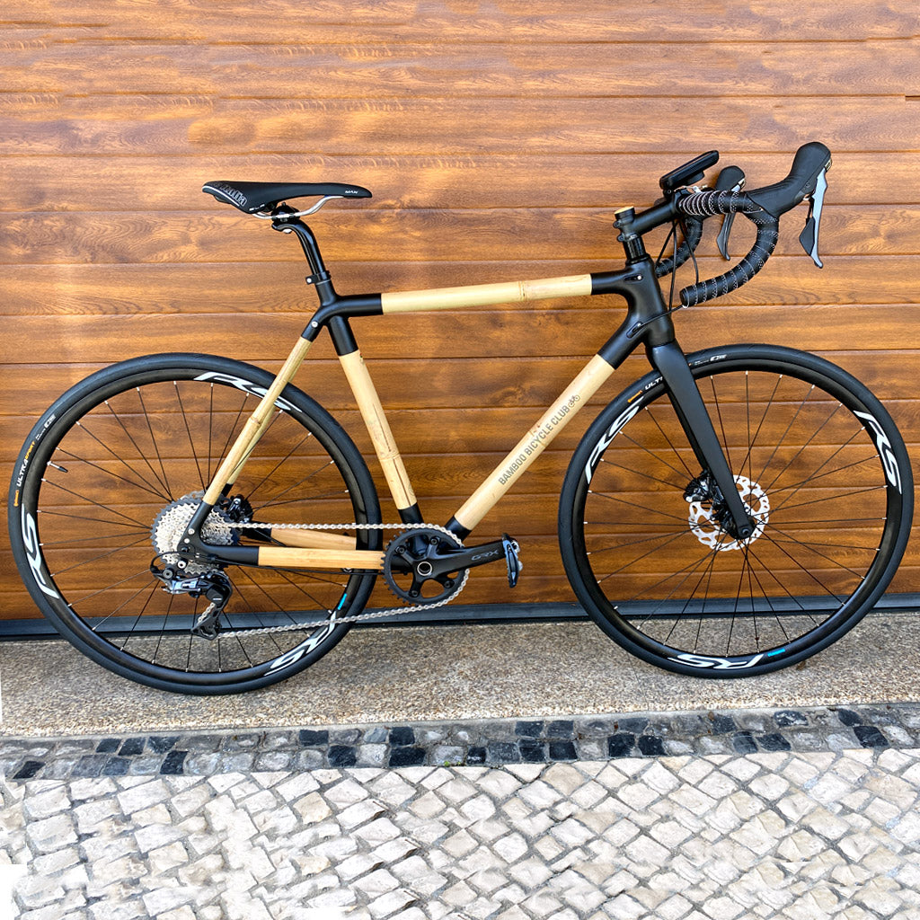 Alcinio's bamboo road bike with black lugs and disc brakes against a wood-panelled wall