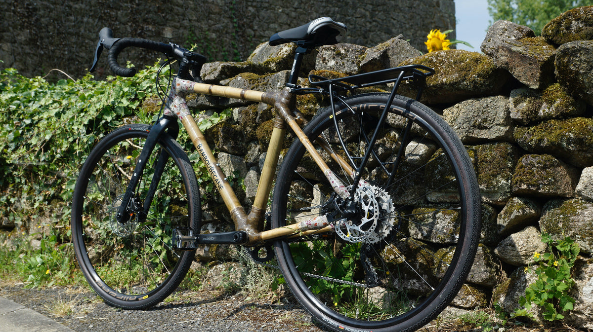 Samuel's bamboo touring bike with patterned wrapped joints and a rear rack against a mossy stone wall