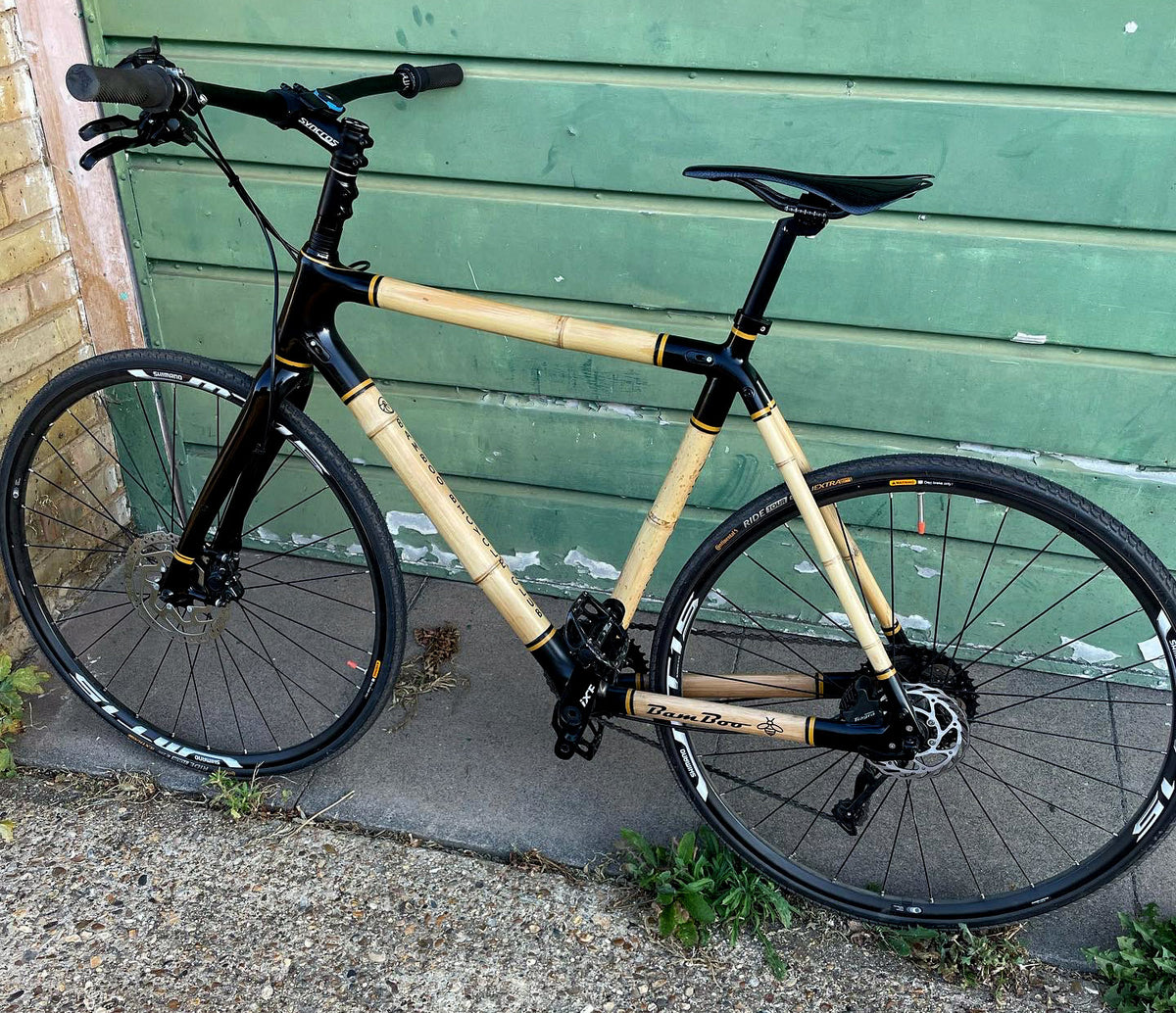 Jon's flat-bar bamboo bike with glossy black lugs and yellow trim, leaning against a green garage door