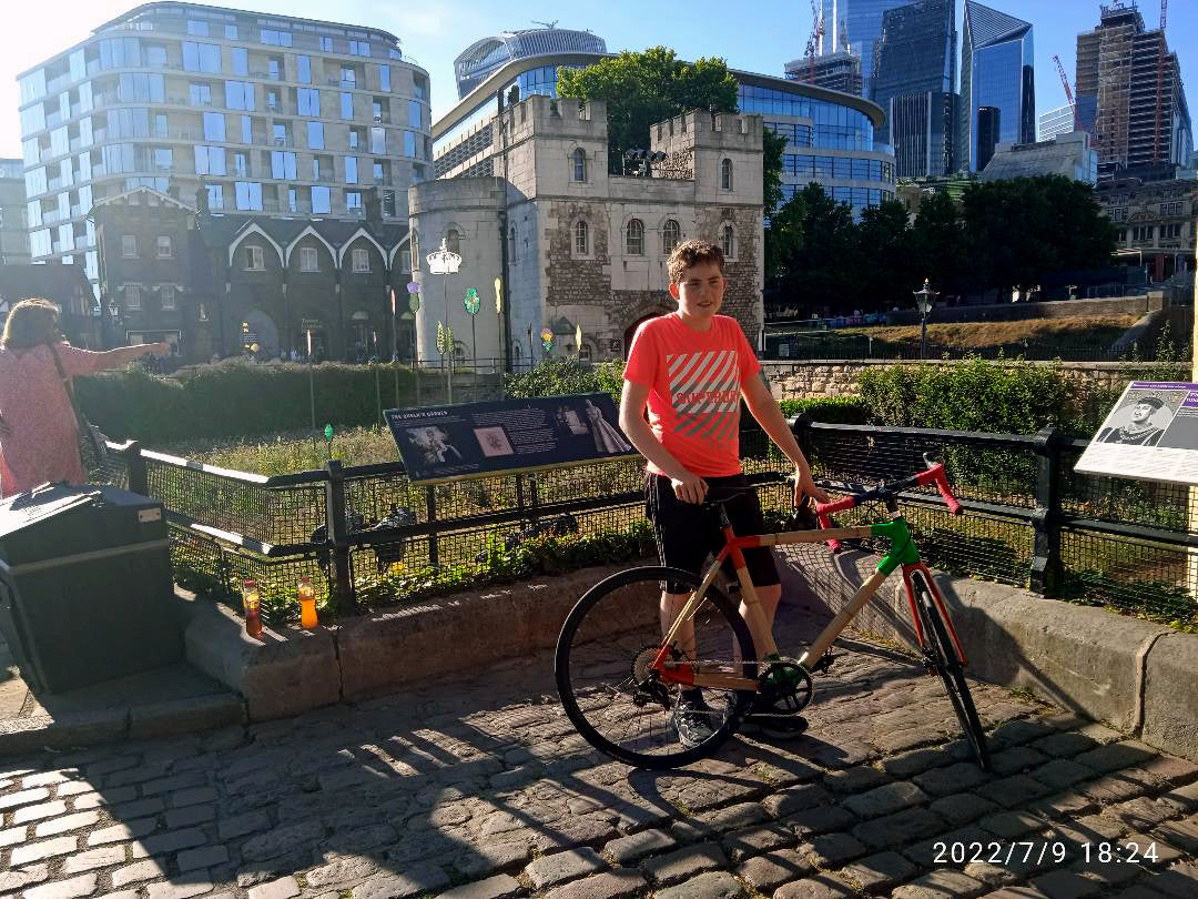 Rider holding Jack's bamboo road bike with a red fork and green head lug by a stone gatehouse