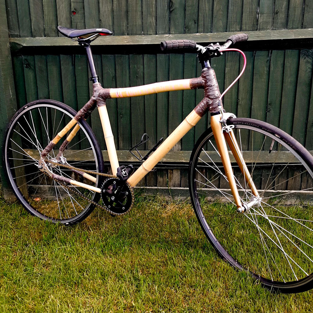 Karl's single-speed bamboo city bike with brown wrapped joints and flat bars on a lawn by a fence