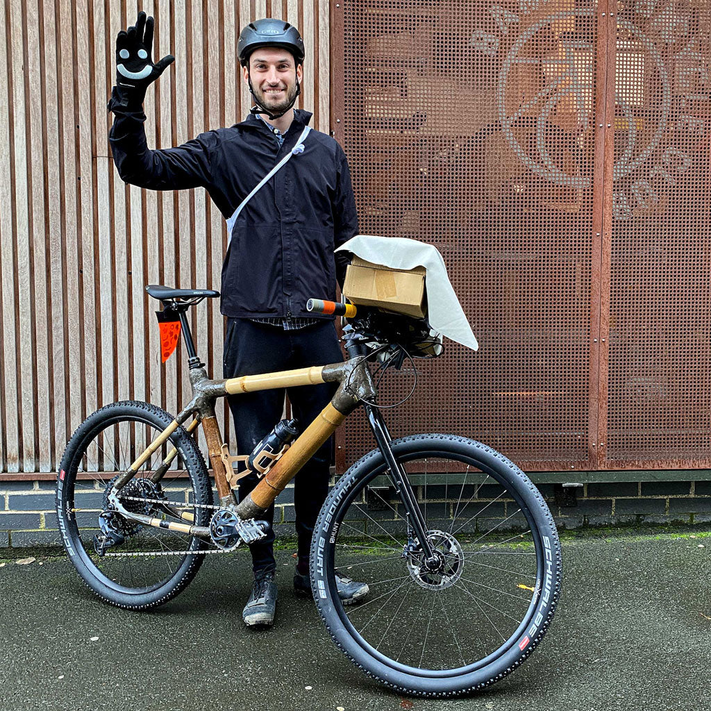 A rider waves from behind Miles's bamboo touring mountain bike, with a cardboard parcel on the front rack