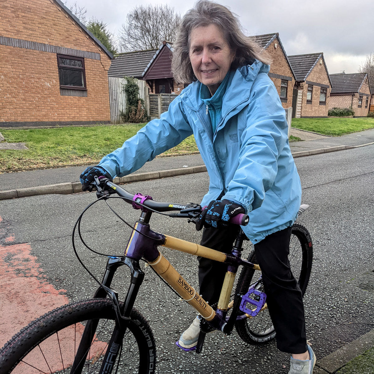 A rider on a bamboo mountain bike with purple joints and 'Bamboo Beauty' lettering, on a residential street