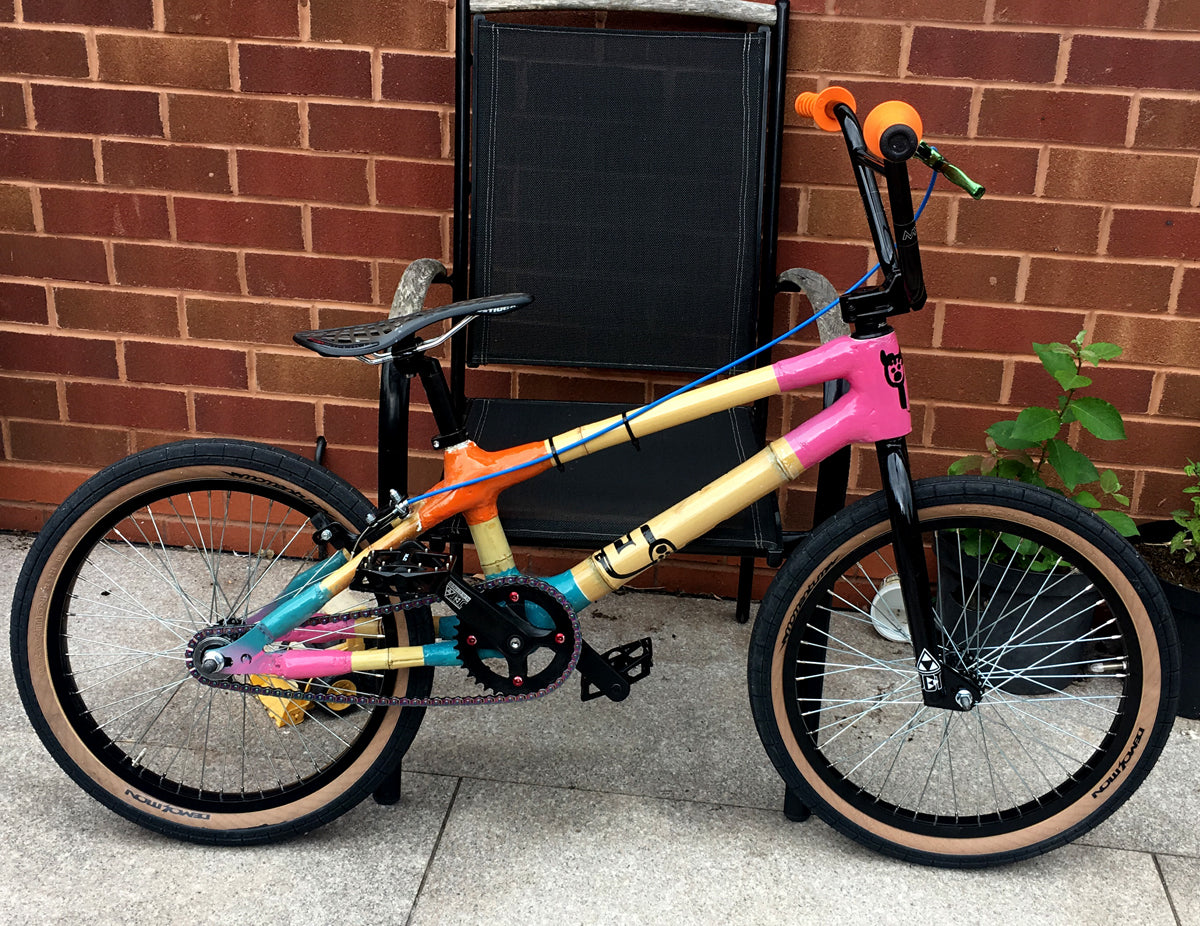 George's bamboo BMX with pink, orange and teal lugs and tan-wall tyres, parked by a brick wall