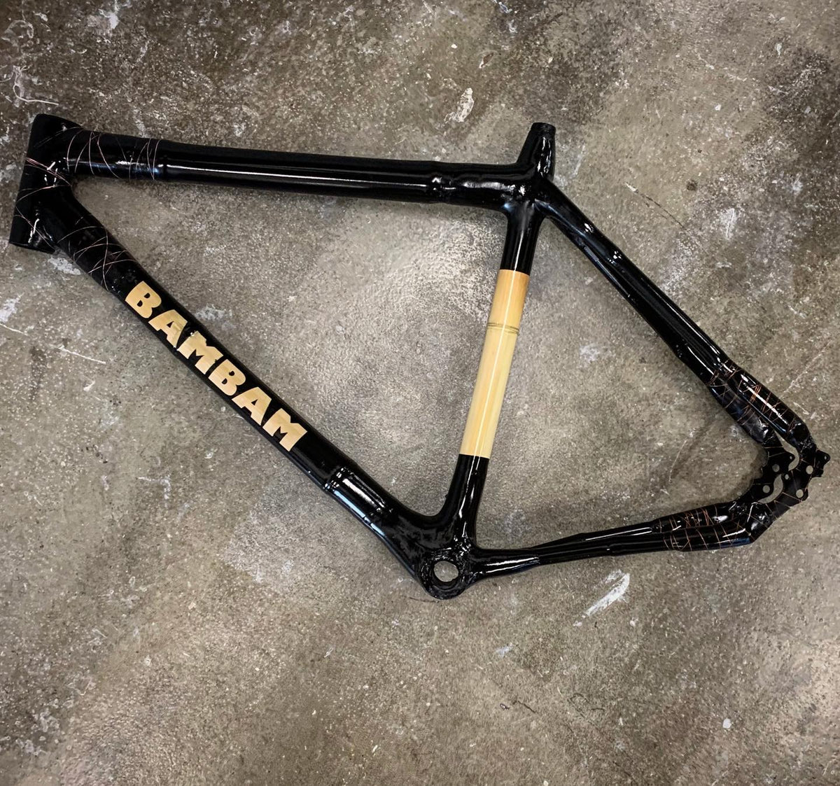 Glossy black-finished frame with 'Bambam' on the down tube and a natural bamboo seat tube, on concrete