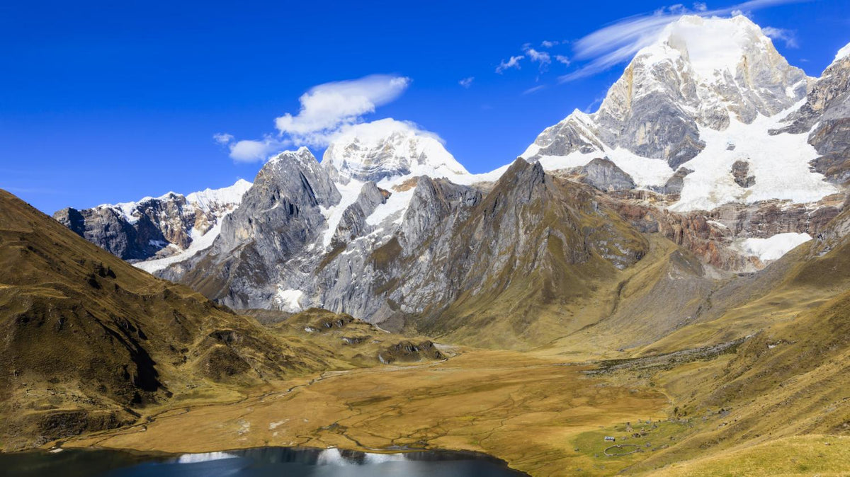 Snow-capped mountains above a golden valley and lake under a deep blue sky in South America