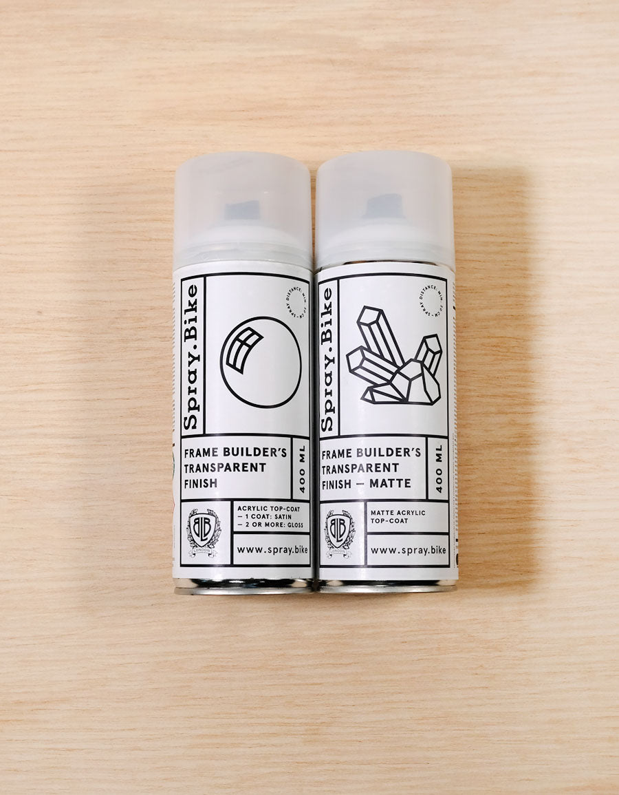 Two 400 ml Spray.Bike frame builder's transparent finish cans, one gloss and one matt, on light wood