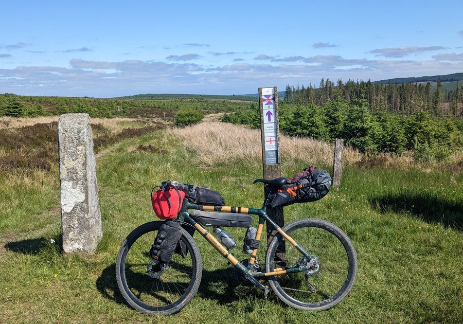 A loaded bamboo touring bike parked beside a waymarker on open moorland