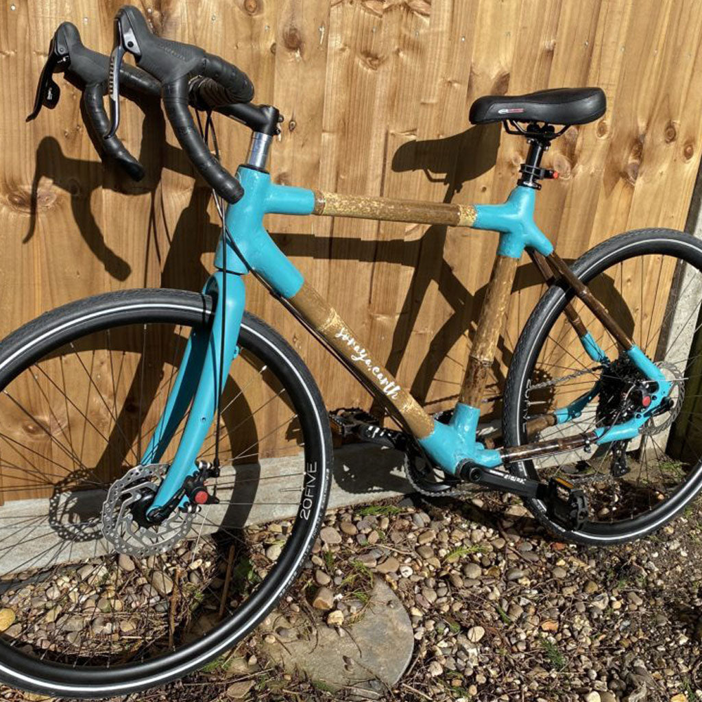 Soraya's bamboo road bike with turquoise joints and fork, leaning against a wooden fence on gravel