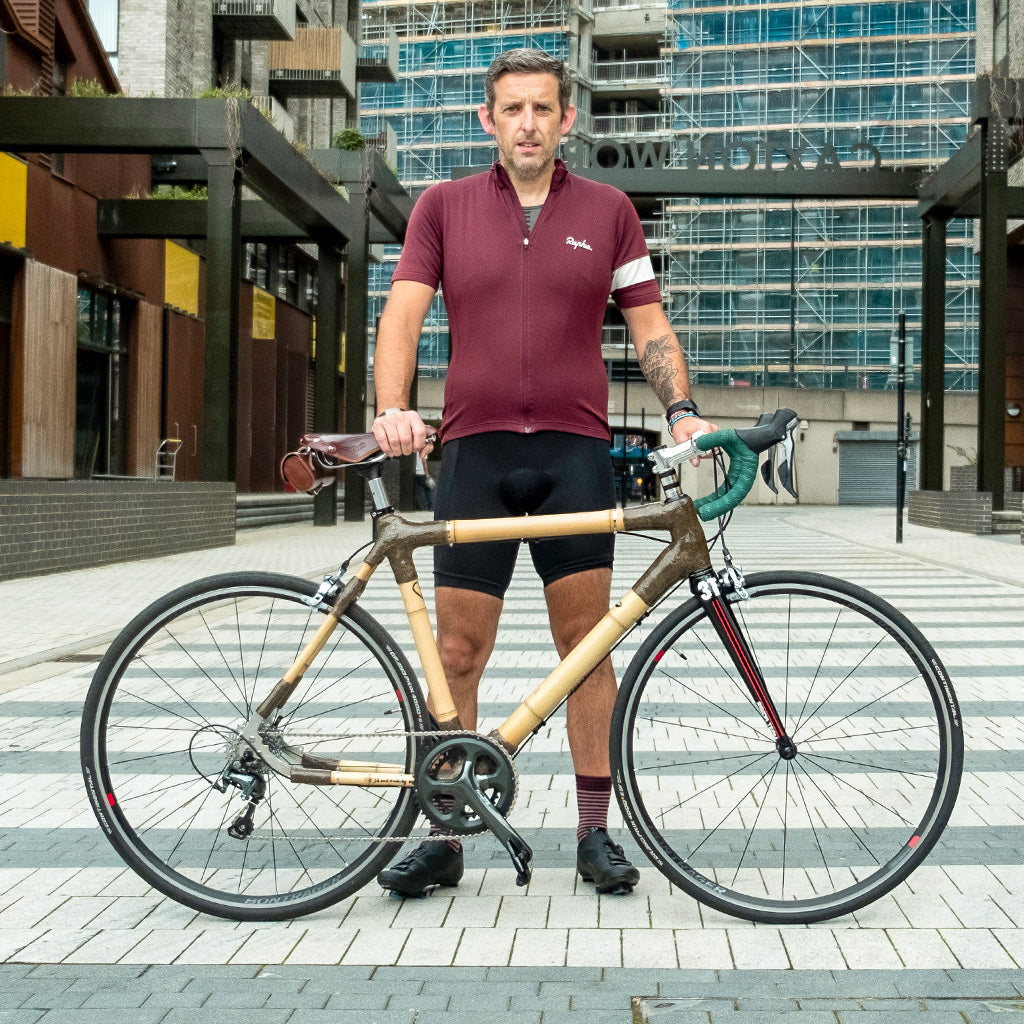 Rider behind Paul's bamboo road bike with a brown saddle and green bar tape in a paved square