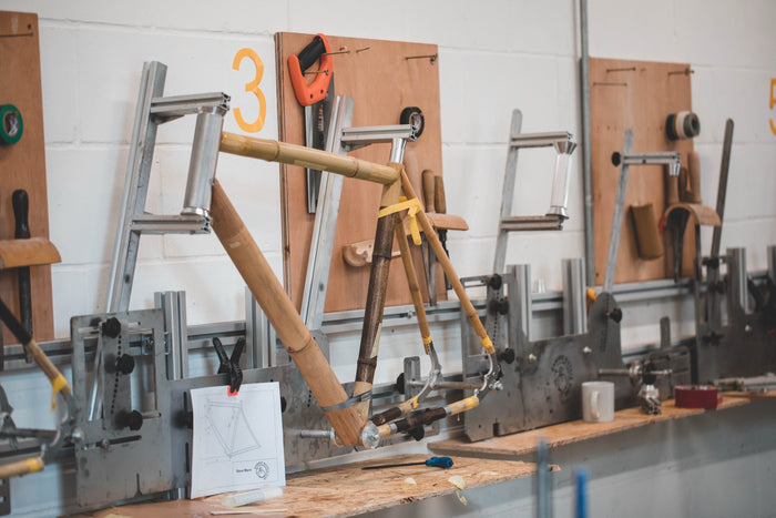 A bamboo bicycle frame clamped in a metal building jig beside its technical drawing