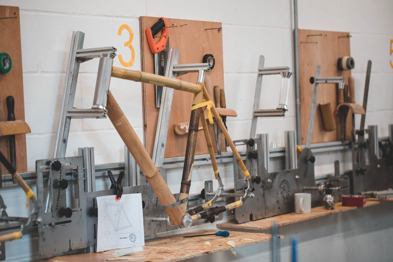 A bamboo bicycle frame clamped in a metal building jig beside its technical drawing