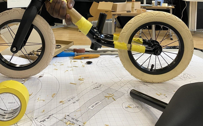 A bamboo balance bike being built over design drawings on a workbench