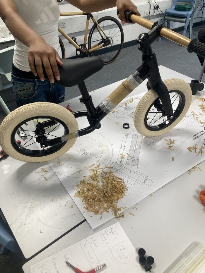 A completed bamboo balance bike resting on the technical build plans at the workshop