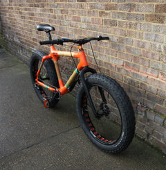Orange bamboo fatbike with huge knobbly tyres against a brick wall