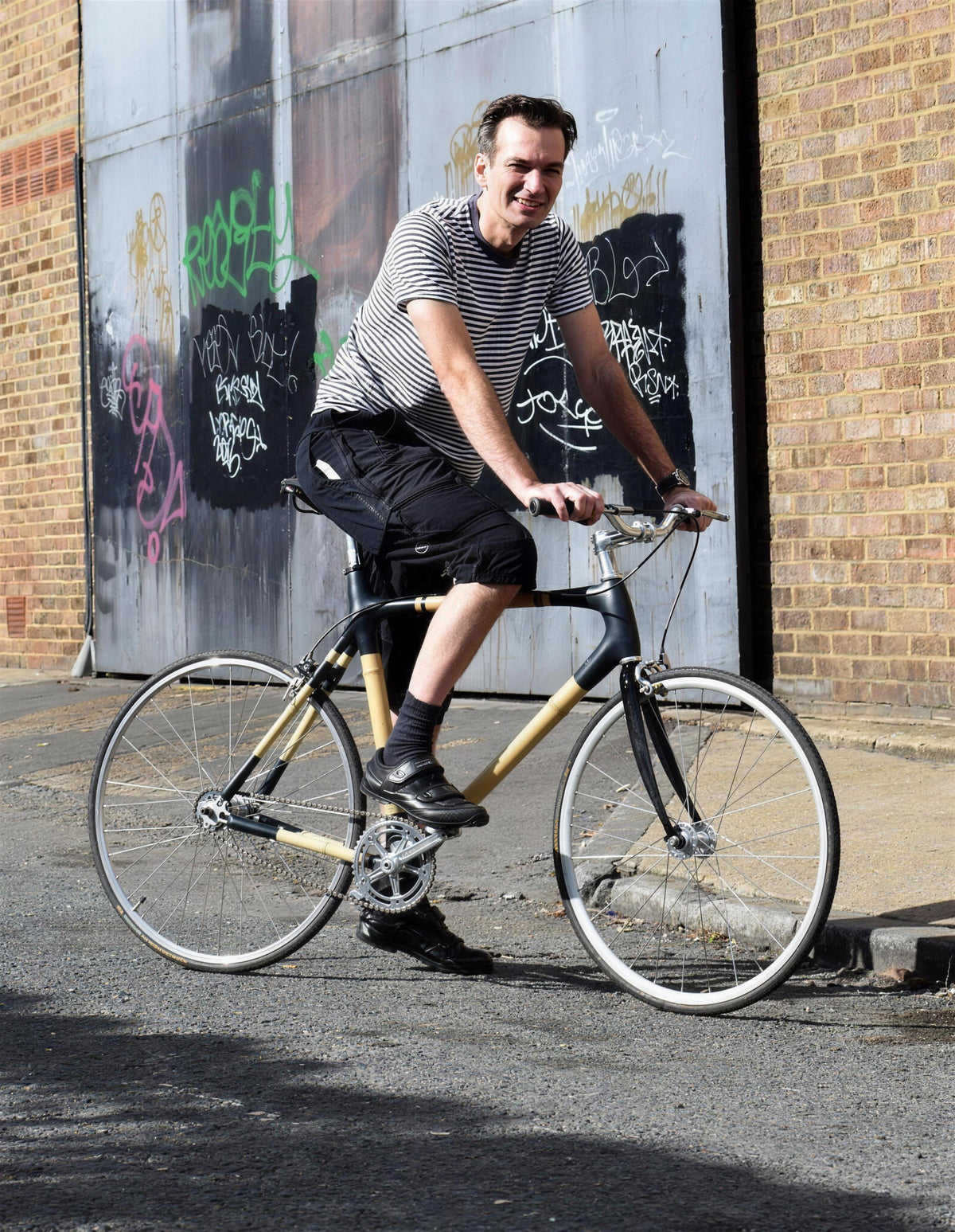 A rider on a bamboo bike riding along a street past a brick building with graffiti-covered doors