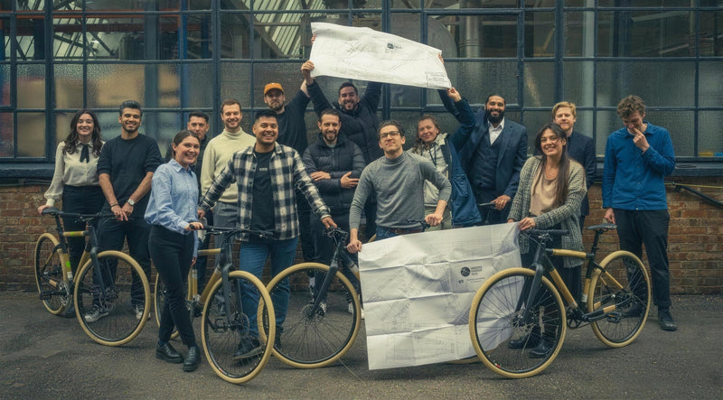 A corporate team holding up their frame drawings beside the bamboo bikes they built on a team day