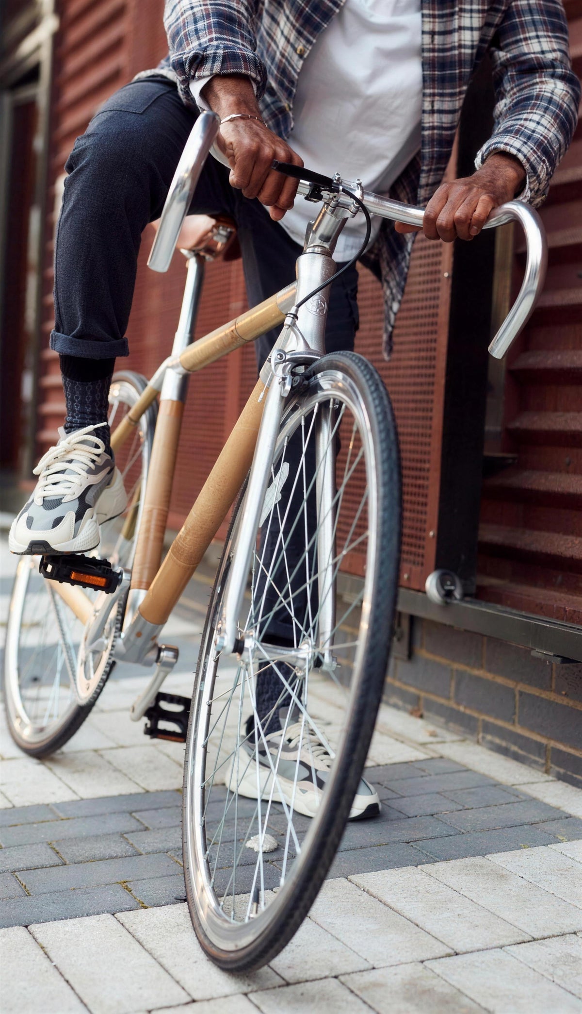 Hands on the drop bars of a bamboo bike, the rider stopped beside a red-panelled wall in the city