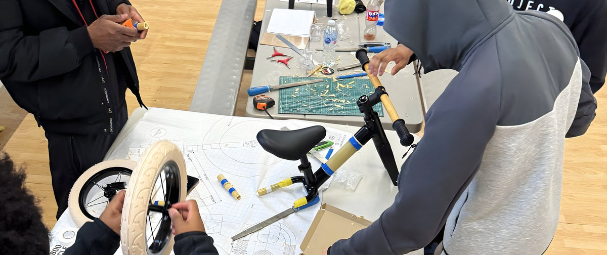 Young people building a bamboo balance bike together on a table covered in drawings