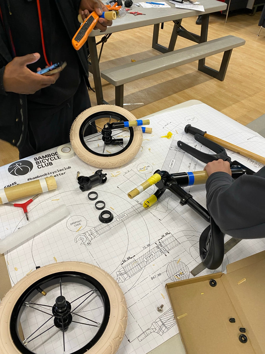 A part-built bamboo balance bike with wheels and components laid out on the build drawing