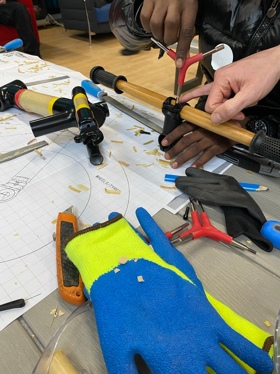Young people's hands shaping a bamboo tube with hand tools on a workbench