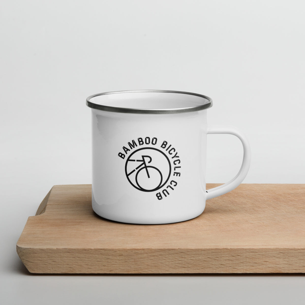 White enamel mug with the circular Bamboo Bicycle Club logo, handle to the right, on a wooden board