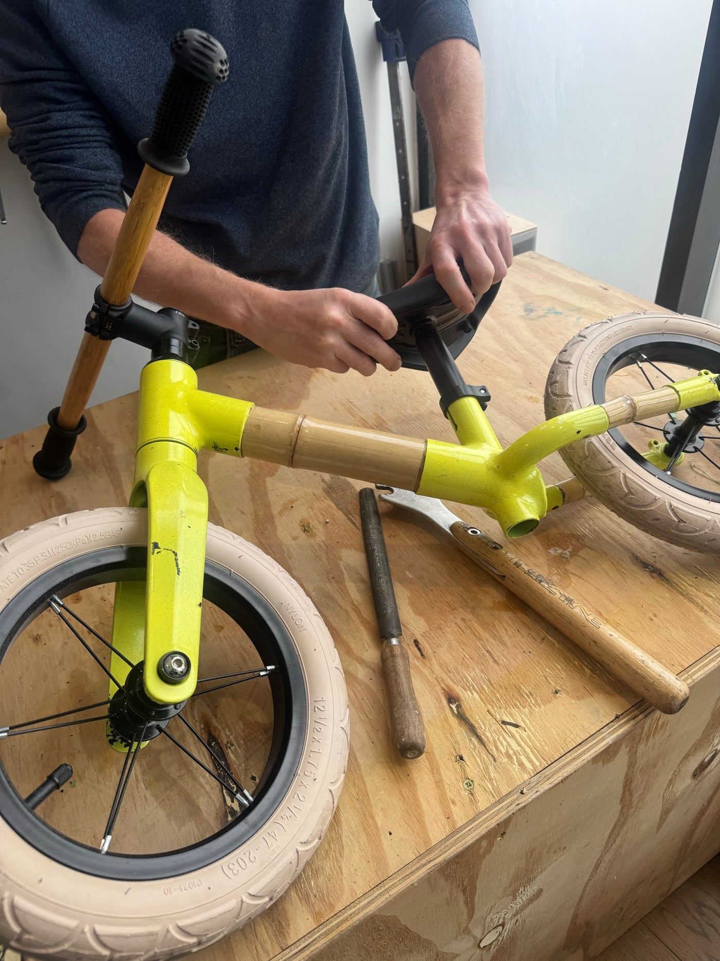 A bamboo balance bike being put together on a workbench, the build used in schools and prisons