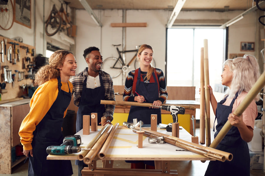 Four colleagues laughing round a build table as they cut bamboo for a frame